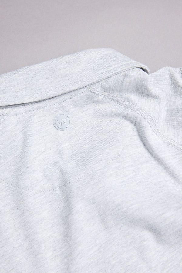 A close-up of the back collar of the WearEver Outbound Polo by WearEver in light gray, showing a subtle embossed circular W logo. The soft, slightly textured fabric is crafted from a breathable cotton-blend.