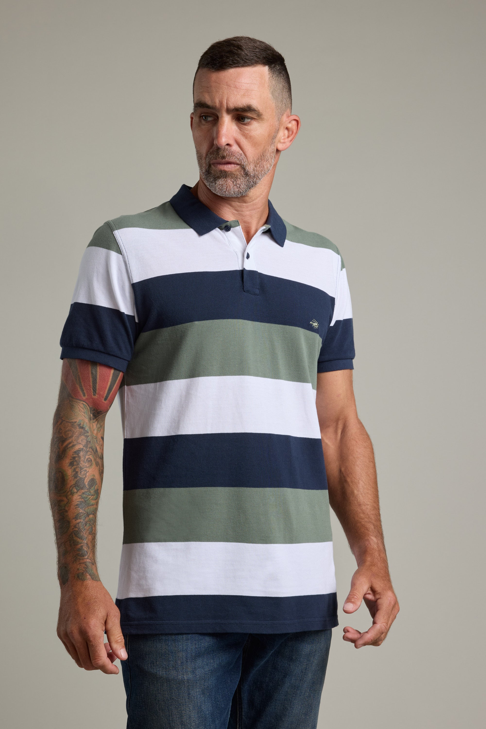 Man wears Barkers Regent Pique Stripe Polo with blue, white, and green bands against plain background.