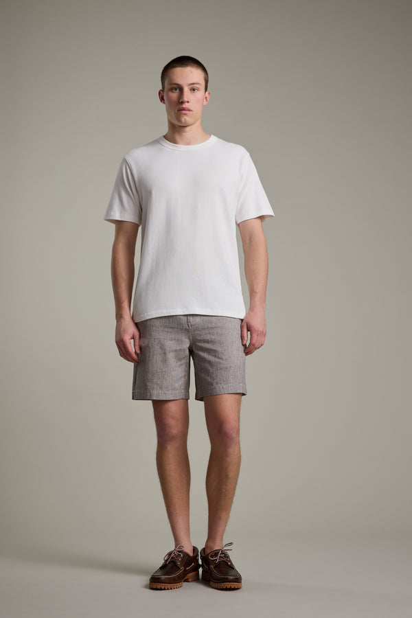 A young man stands facing forward against a light gray background, wearing Barkers' Woodley Weekend Short with an elastic waistband, a plain white T-shirt, and brown shoes. He has short hair and a neutral expression, arms relaxed at his sides.