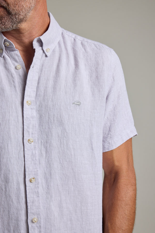 A man wears the Barkers Gentry Linen Shirt, a light short-sleeve style with cream buttons and a crayfish embroidery on the chest. The image shows him from shoulders to mid-torso against a plain, neutral background.