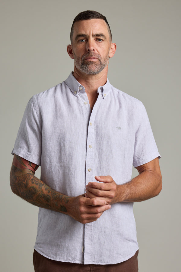 A man with short hair and a trimmed beard stands facing forward, wearing the Barkers Gentry Linen Shirt in light gray. He has a tattoo on his left forearm and holds his hands together in front of him against a plain background.