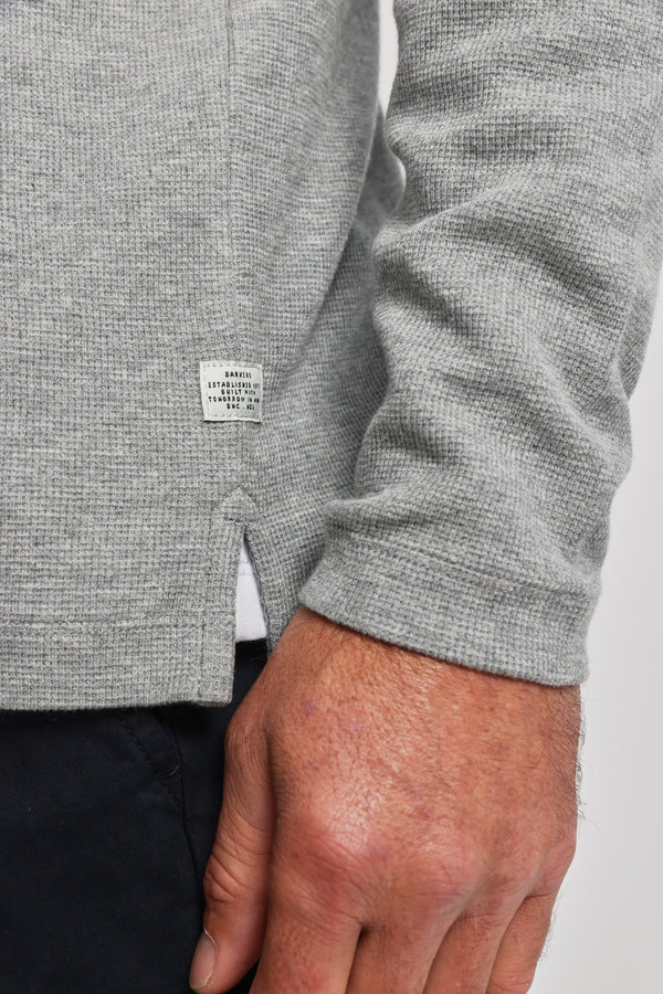 Close-up of a person wearing Barkers’ Avenue Waffle Henley in light gray, featuring a subtle waffle texture, small white tag near the split hem, and paired with dark pants. The person's hand rests casually by their side.