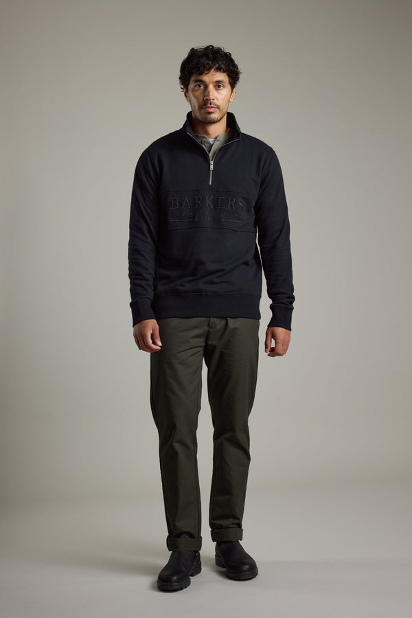 Man in studio wearing Barkers Heritage 1/4 Zip sweatshirt, olive pants, and black shoes.