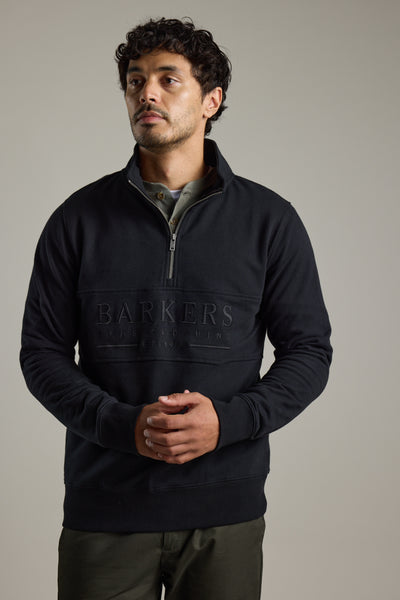 Man in Barkers Heritage 1/4 Zip sweater and olive pants, standing with hands clasped.