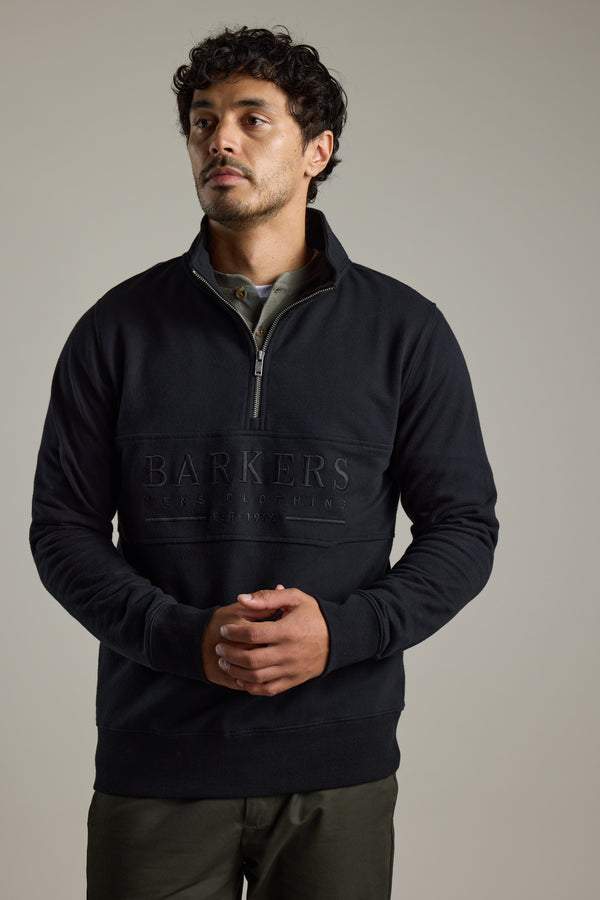 Man in Barkers Heritage 1/4 Zip sweater and olive pants, standing with hands clasped.