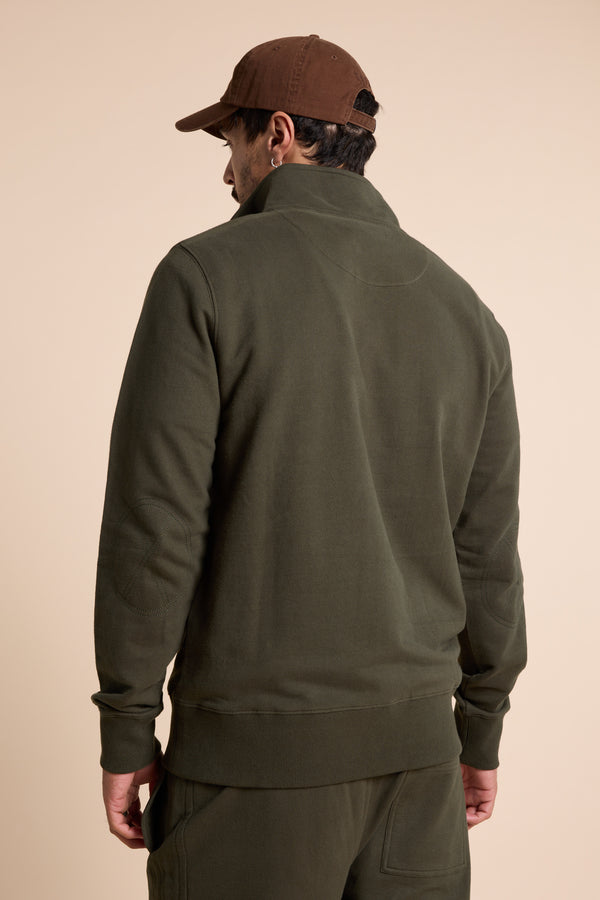 Man in a Barkers Heritage 1/4 Zip sweater and brown cap, seen from behind on beige background.