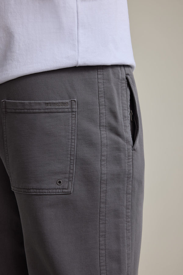 Close-up of a person wearing Barkers Organic Classic Print Track Pant in gray with a white shirt, highlighting the side and back pocket details of these 90s-inspired trackies.