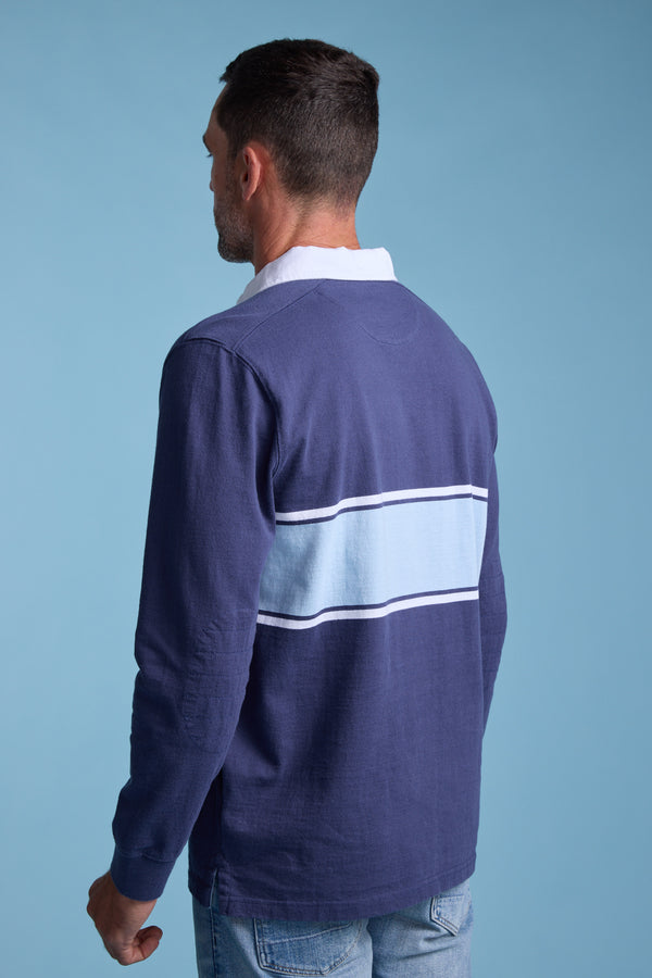 A man with short dark hair, wearing the Barkers Breaker Rugby Jersey in blue with white and light blue stripes across the back, stands facing away against a plain light blue background.