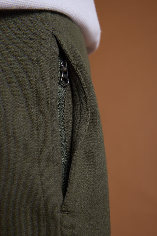 Close-up of a green zippered pocket on the Barkers Heritage Track Pant by Barkers, with part of a white shirt at the top set against a brown background.