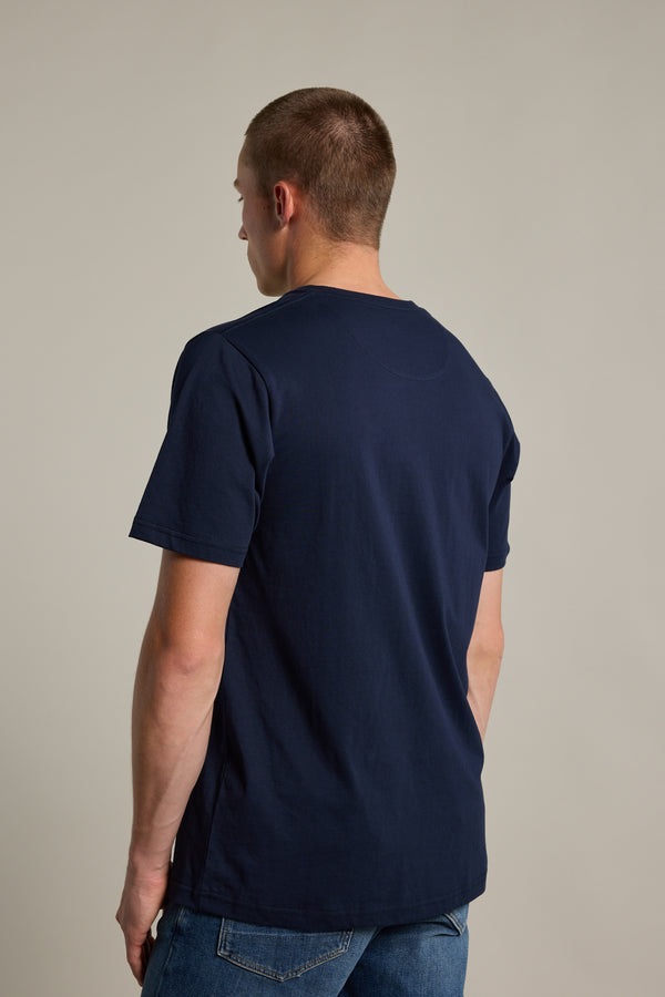 A person with short hair faces away, displaying the back of the Barkers Organic Crew Tee in navy blue with blue jeans against a plain, light background.