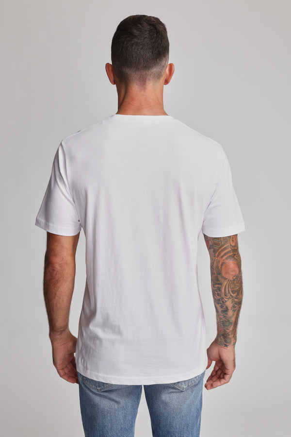 A man with short dark hair, wearing a plain white Barkers Organic Crew Tee and blue jeans, stands with his back to the camera. His right arm is tattooed, set against a neutral light gray background.