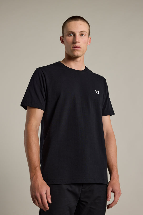 A young man with short hair wears the Barkers Newton Washed Tee—an oversized black t-shirt with a small white logo on the chest—standing against a neutral background and looking directly at the camera.