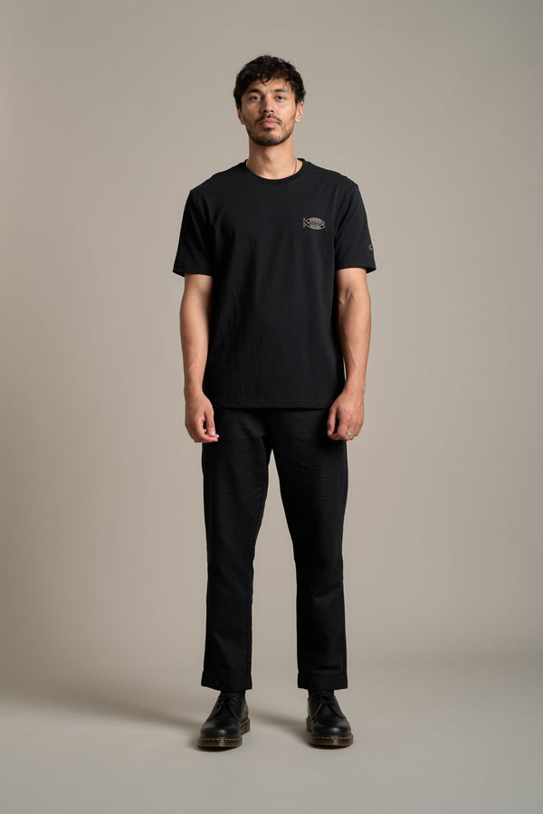 A man with short dark hair and light facial hair stands against a plain background, wearing the Legasea Crayfish Print Tee by Legasea. He faces forward with a neutral expression, paired with black pants and shoes.