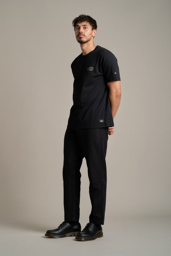 A man with short dark hair and a slight beard stands against a beige background, wearing LegaSea’s Crayfish Print Tee, made from organic cotton, showing his support for New Zealand marine conservation.