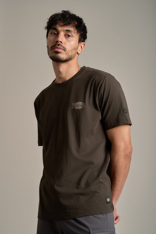 A man with short curly hair and a trimmed beard wears the Legasea Crayfish Print Tee by Legasea, an organic cotton t-shirt featuring a small crayfish graphic, standing against a plain light background and looking slightly upward with a relaxed expression.