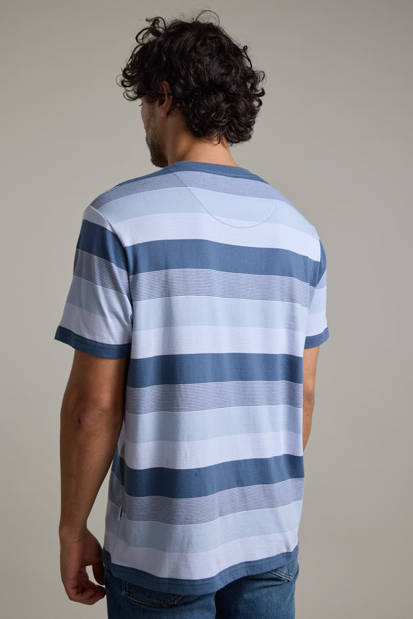 A man with curly dark hair, wearing the Barkers Fitzroy Stripe Tee and jeans, stands facing away from the camera against a plain background.