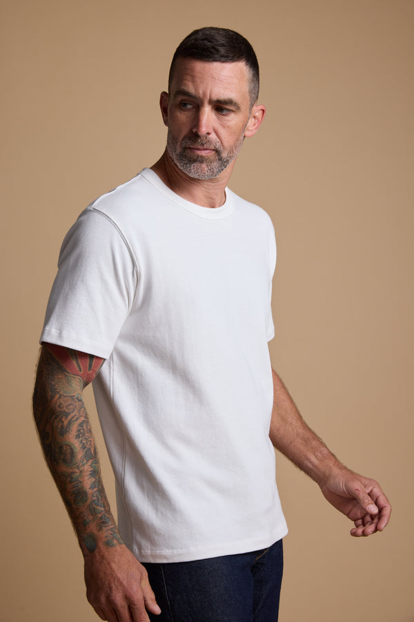 Tattooed man with short hair wears the Barkers Langwood Tee against a beige background.