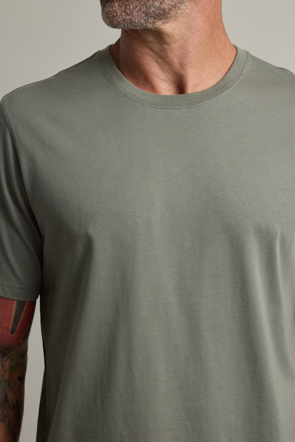 Man in a Barkers Good Earth Cotton Essential Tee, sage green, tattooed arm partly visible.