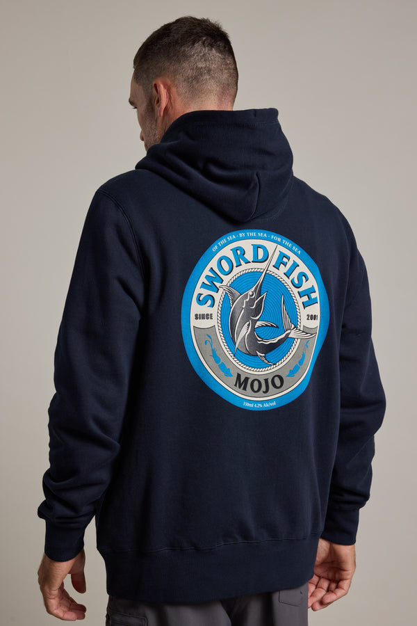 A man wearing a dark Swordfish Mojo Logo Hoody made from responsibly sourced cotton stands with his back to the camera, displaying the Swordfish Mojo brand’s large circular logo featuring a jumping swordfish and blue accents since 2001.