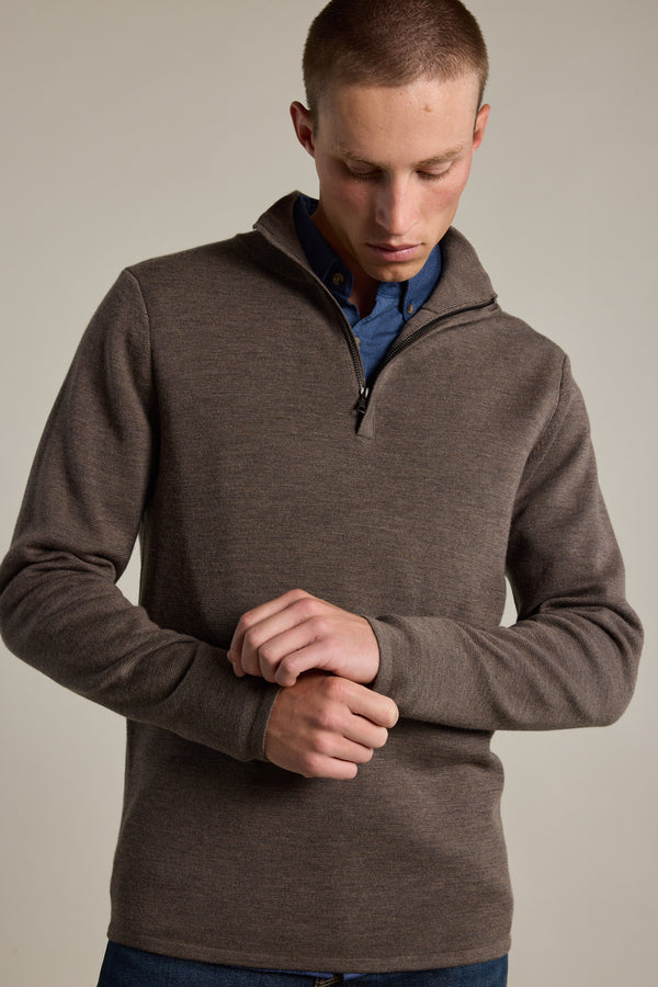 A person wears the Barkers Brandon ZQRX Merino 1/4 Zip sweater in brown over a blue shirt, adjusting their sleeve against a plain background—an ideal layering piece for versatile style.