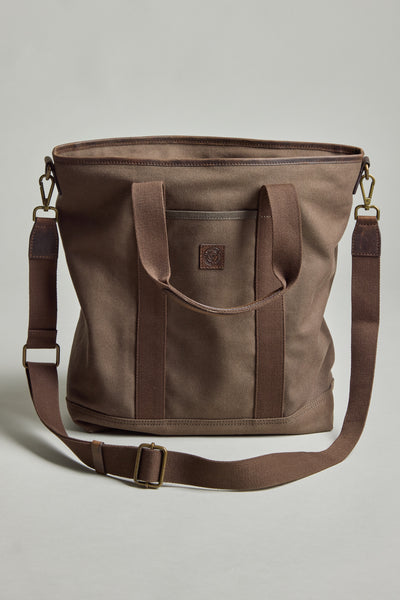 The Barkers Foxton Canvas Convertible Tote is a brown cotton canvas bag with two short handles, an adjustable shoulder strap, a small front pocket, brass hardware, and a minimalist design.