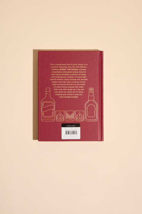 A red hardcover "Whisky The Manual" by Other lies flat, displaying its back cover with gold outlines of two liquor bottles and three whiskey glasses, plus a text block and barcode on a beige background for a whisky guide feel.