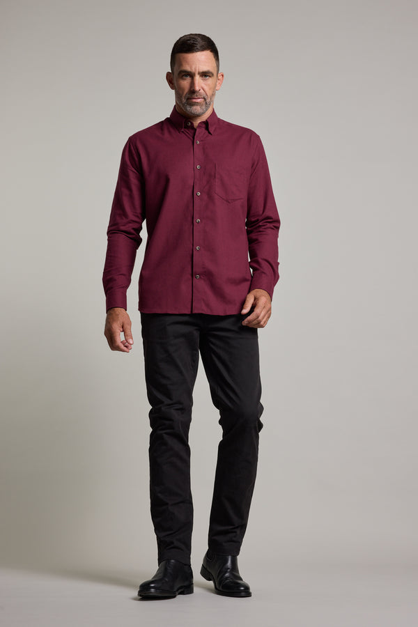 A man with short dark hair and a neutral expression wears a long-sleeved maroon Barkers Antonio Shirt in classic fit, paired with black pants and dress shoes, standing against a plain background.