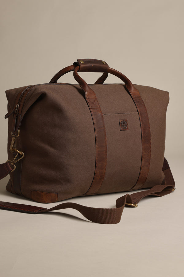 The Barkers Newman Canvas Weekender is a brown travel bag with leather handles and a detachable shoulder strap, displayed on a plain beige background.
