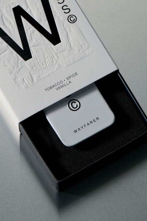 A white rectangular Solid State - Wayfarer device with a large W sits in a black foam-lined box; the packaging highlights TOBACCO • SPICE VANILLA, indicating a wax-based solid cologne by Solid State.