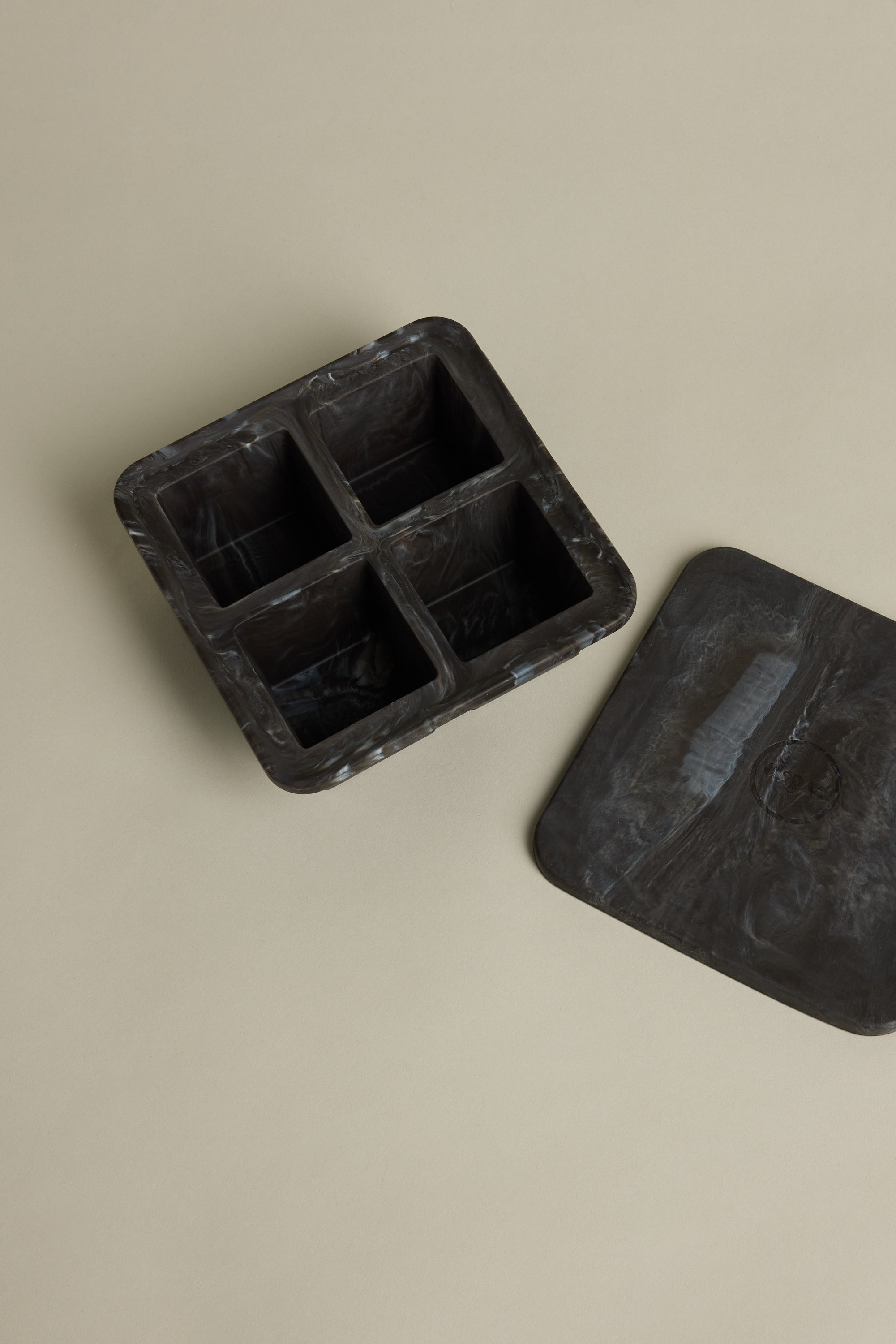 The Other Ice Tray Sphere Marble Black features four compartments for slow-melting ice cubes and comes with a matching flat lid. Shown on a beige surface, it’s ideal for any home bar setup.