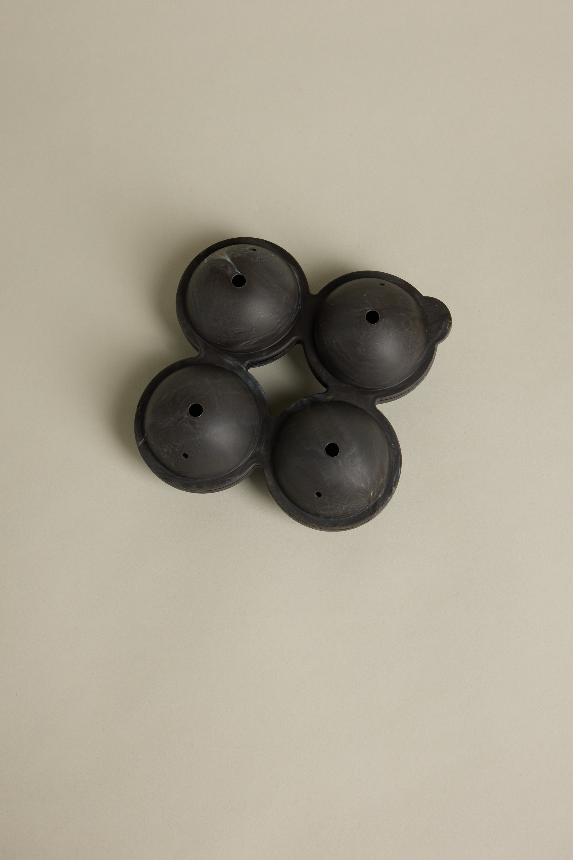 Four Barkers Ice Tray Sphere Marble Black molds, round with small center holes, are interconnected in a square on a beige background—perfect for making large cocktail ice spheres.