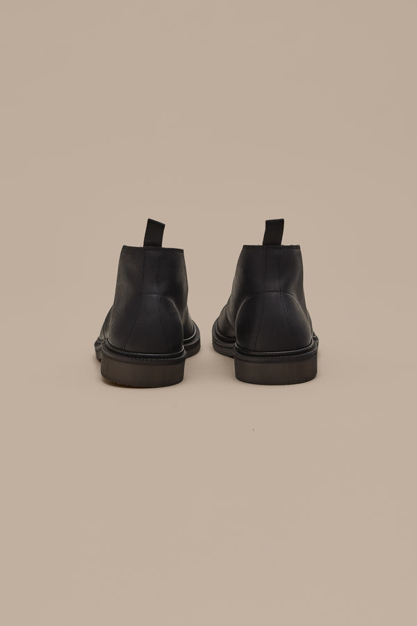 The Barkers Howarth Desert Boot in black leather is displayed from the back, featuring pull tabs on each heel and set against a plain beige background.