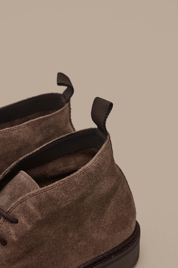 Close-up of the back of Barkers’ Howarth Desert Boot in brown suede with black pull tabs, set against a beige background, highlighting its classic style.