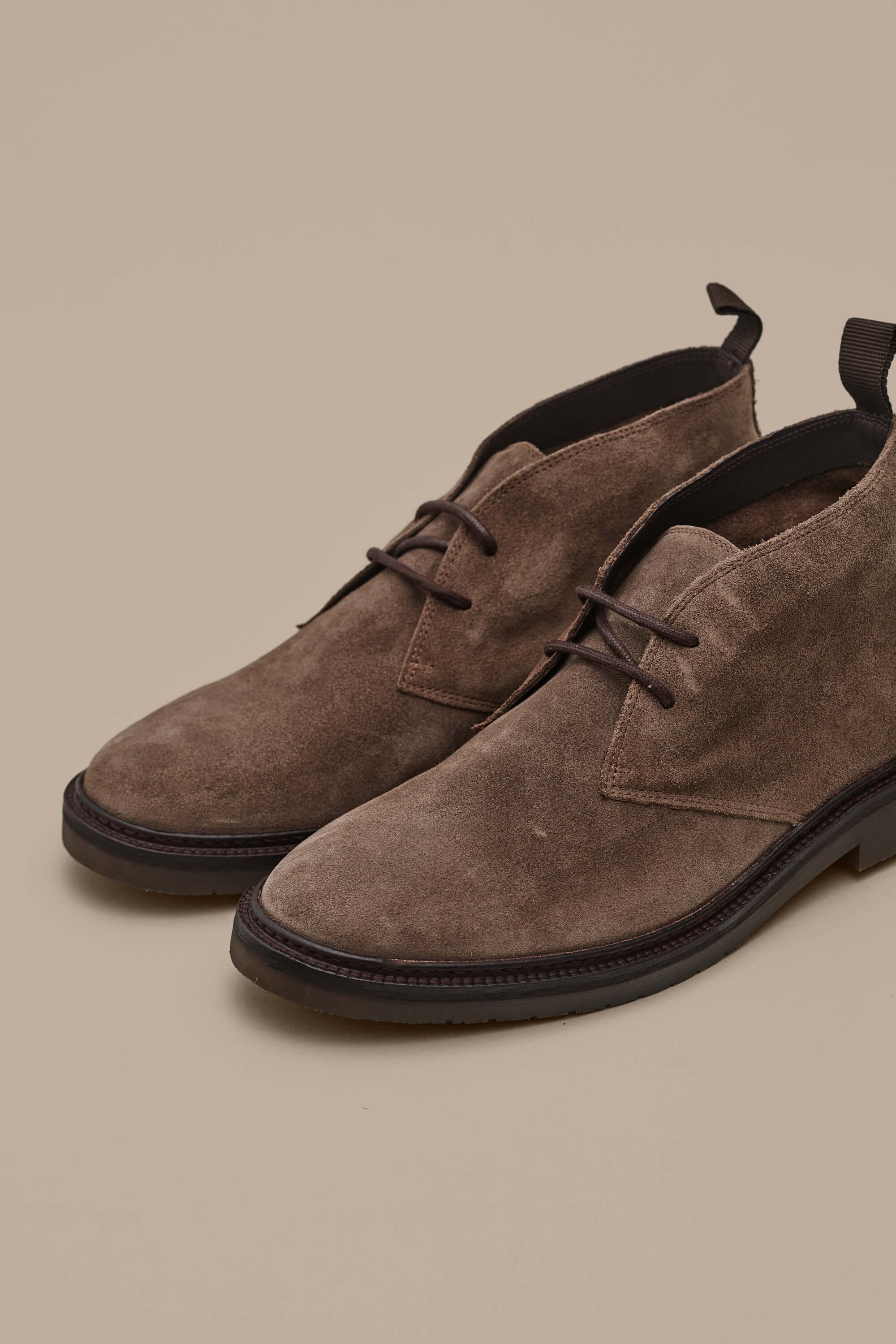 The Barkers Howarth Desert Boot, a quality brown suede pair with dark brown soles and pull tabs, is displayed on a beige background.