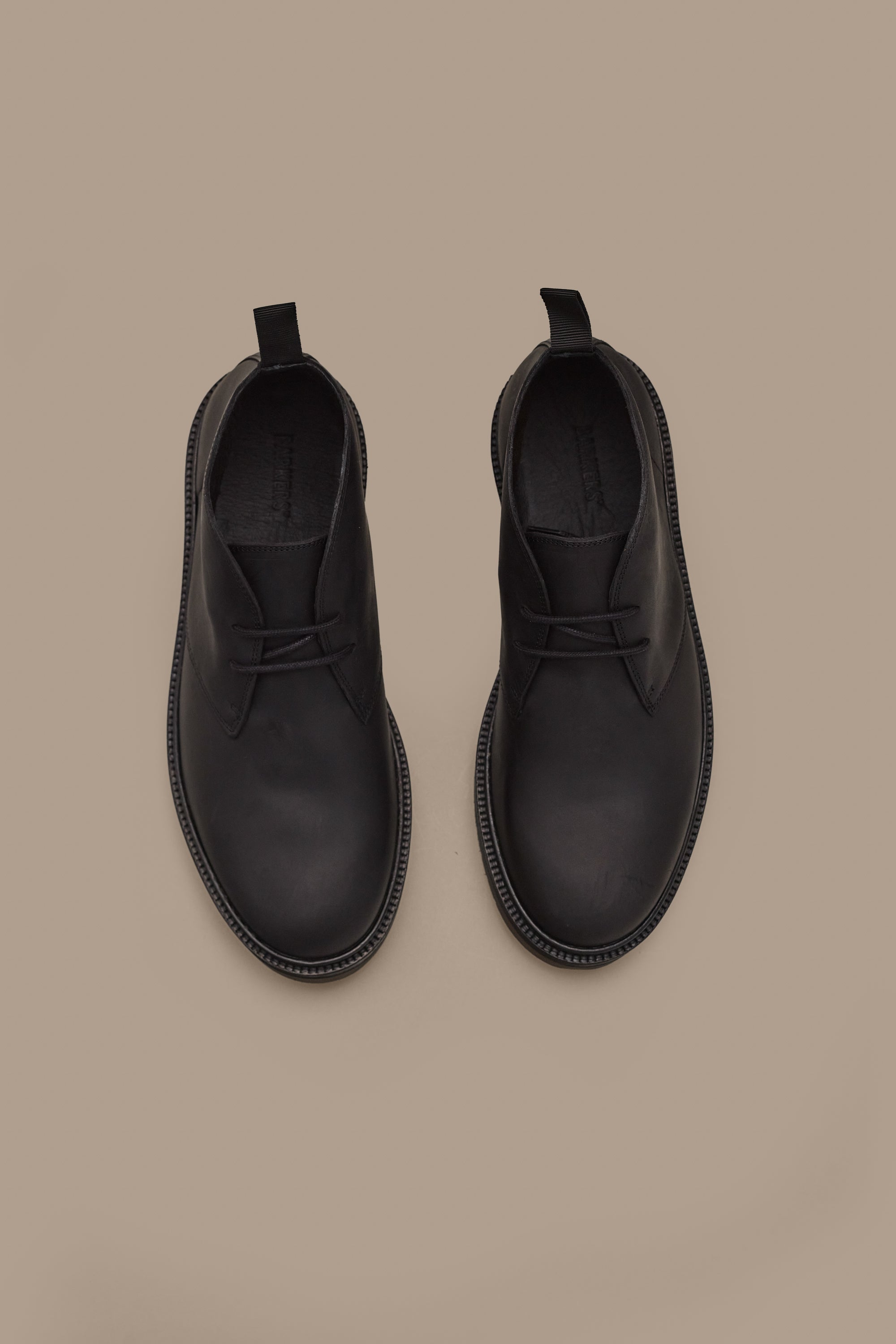 The Howarth Desert Boot by Barkers—black leather boots with laces and pull tabs in classic Portuguese style—are displayed side by side on a plain beige background.