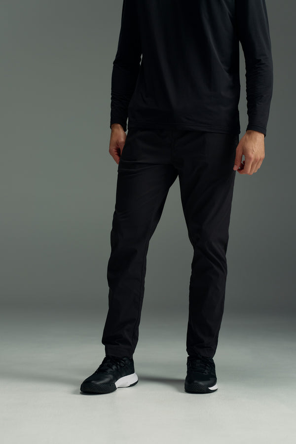 A person stands on a gray floor wearing a long-sleeve black shirt, WearEver Transit Pant by WearEver, and black athletic shoes. The upper part of their head is not visible in the image.
