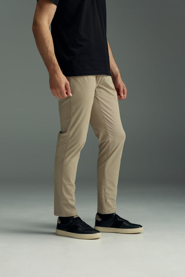 A person models WearEver's Long Game Pant—a chino-inspired, lightweight performance style—paired with a black T-shirt and black sneakers. They stand against a plain gray background, arms relaxed; the photo is cropped at the shoulders.