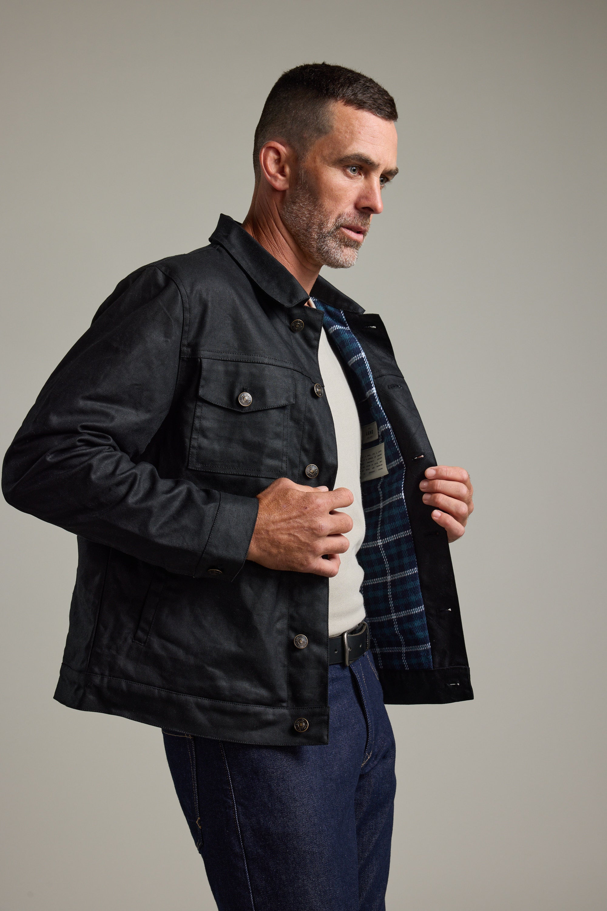Man in Barkers Benson Waxed Cotton Jacket shows its plaid inner lining while wearing jeans.