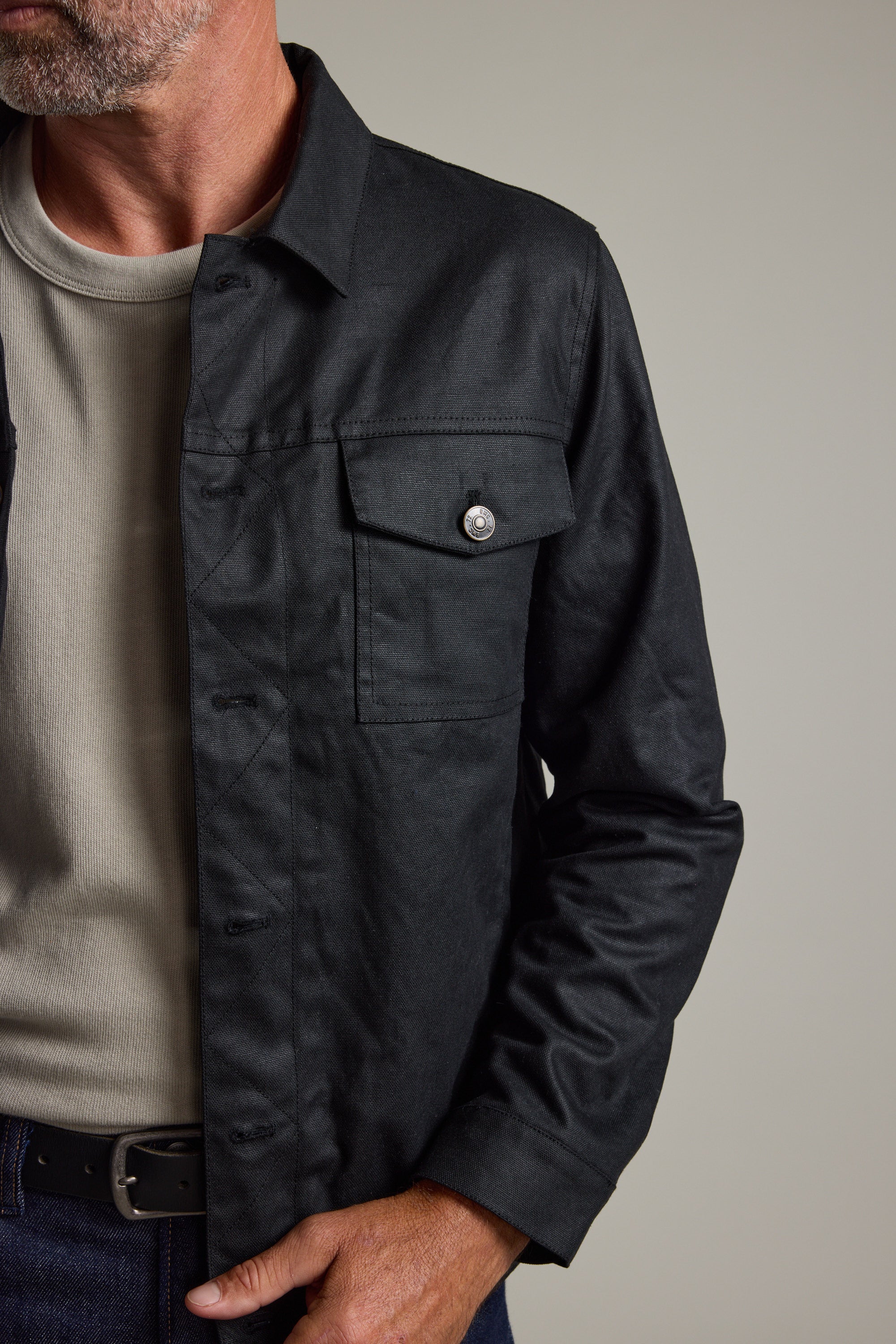 Man wears Barkers Benson Waxed Cotton Jacket over a beige tee, hand casually in pocket.