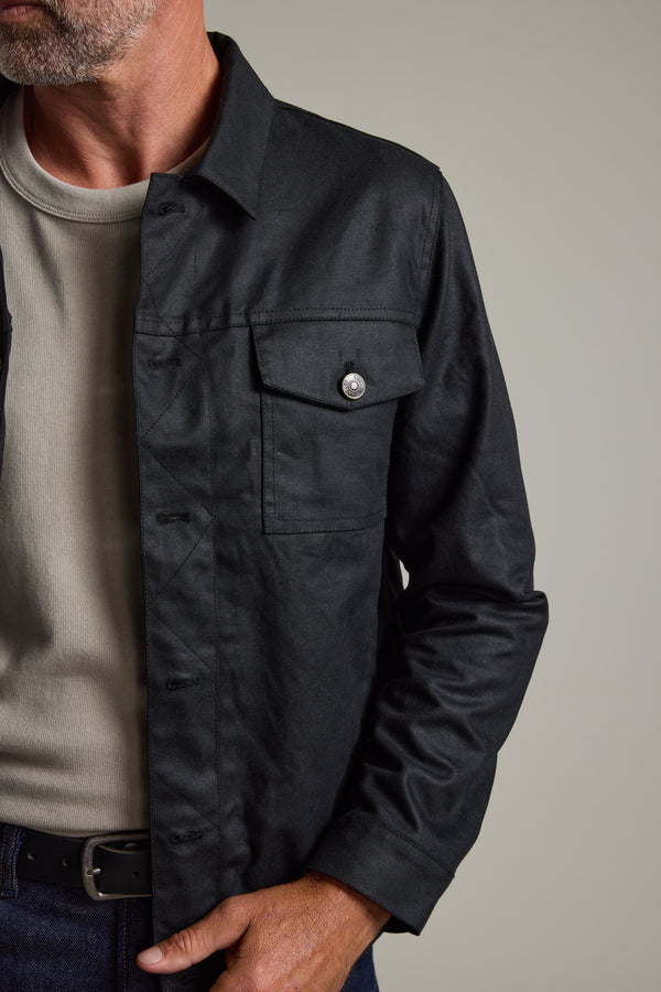 Man wears Barkers Benson Waxed Cotton Jacket over a beige tee, hand casually in pocket.