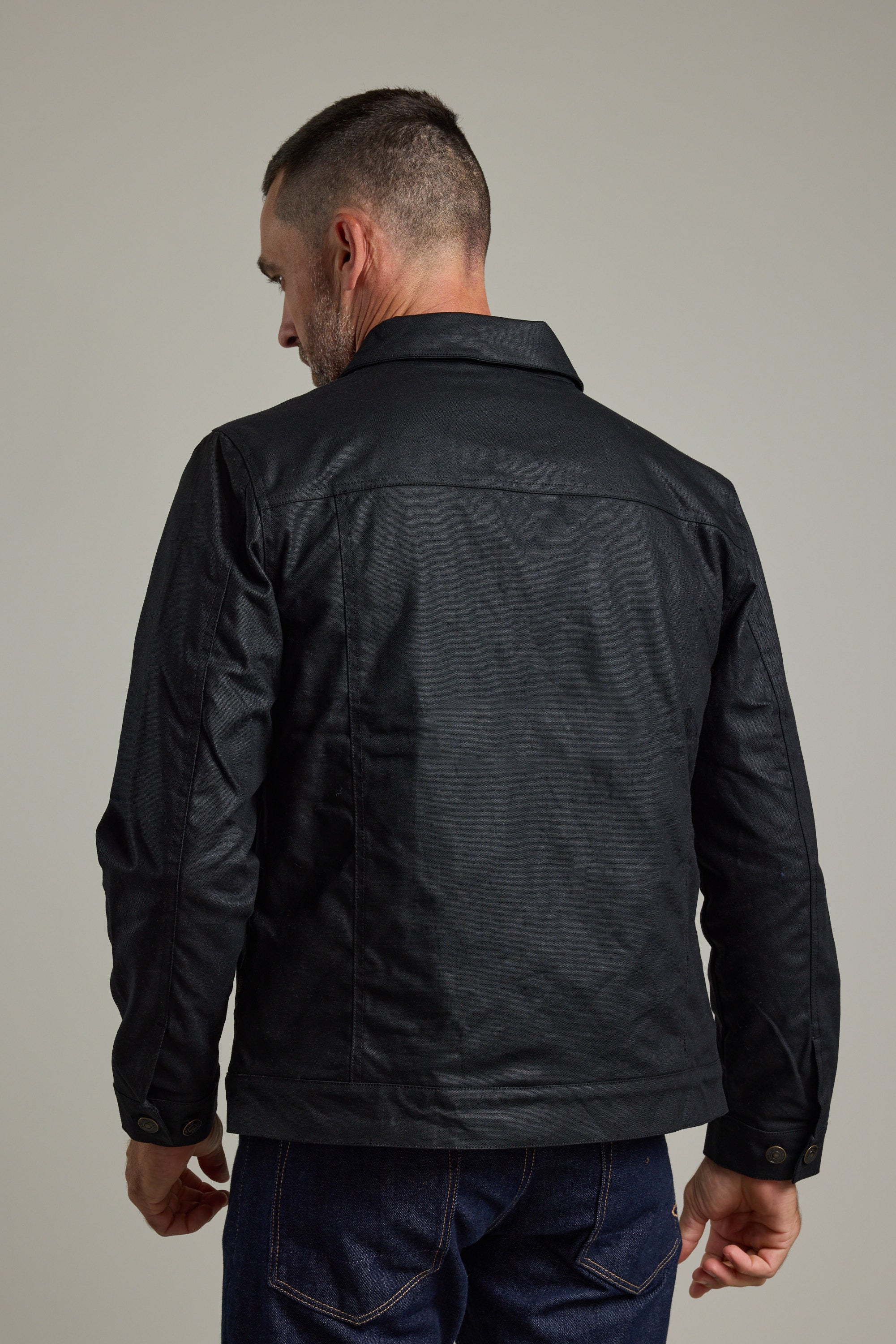 A man in a Barkers Benson Waxed Cotton Jacket and dark jeans, shown from behind.