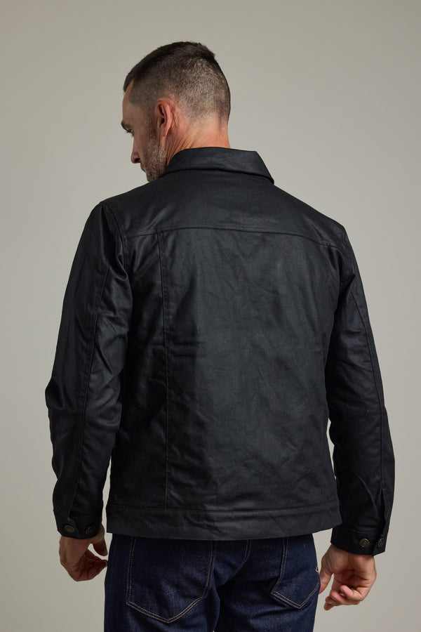 A man in a Barkers Benson Waxed Cotton Jacket and dark jeans, shown from behind.