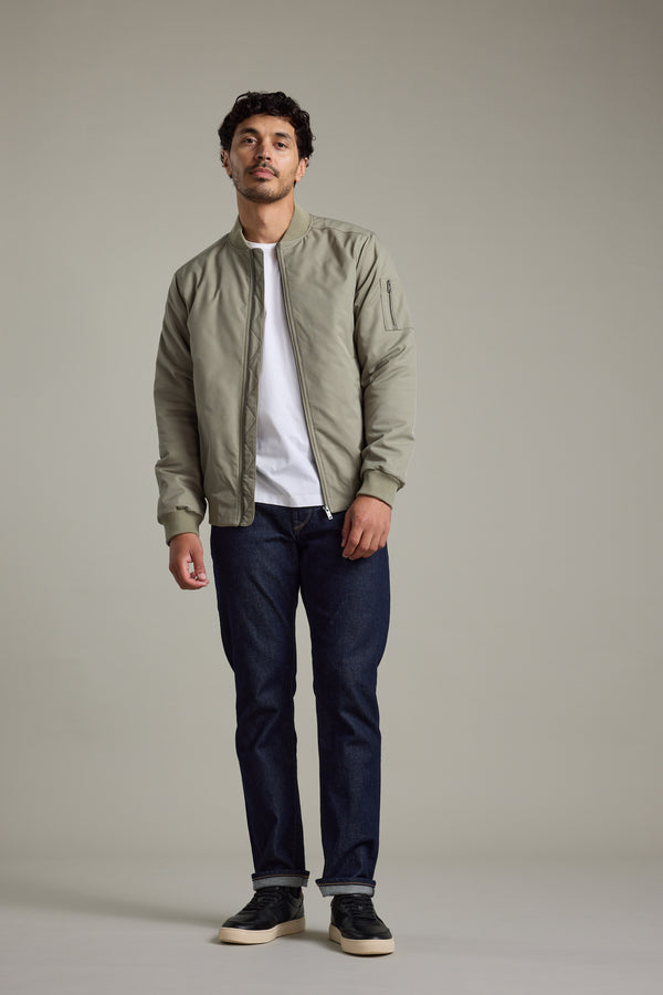 Man in Barkers Dunhill Bomber Jacket, white shirt, jeans, and sneakers on plain background.