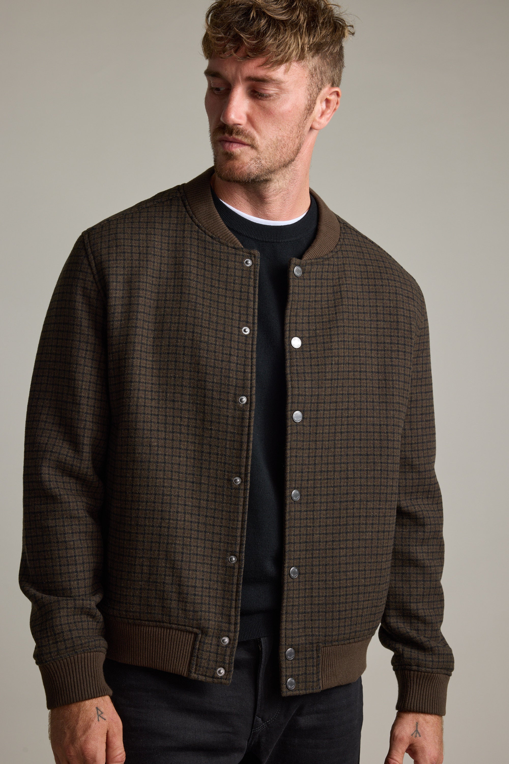 Man in Barkers Leland Wool Bomber Jacket over a black shirt, looking down to the side.