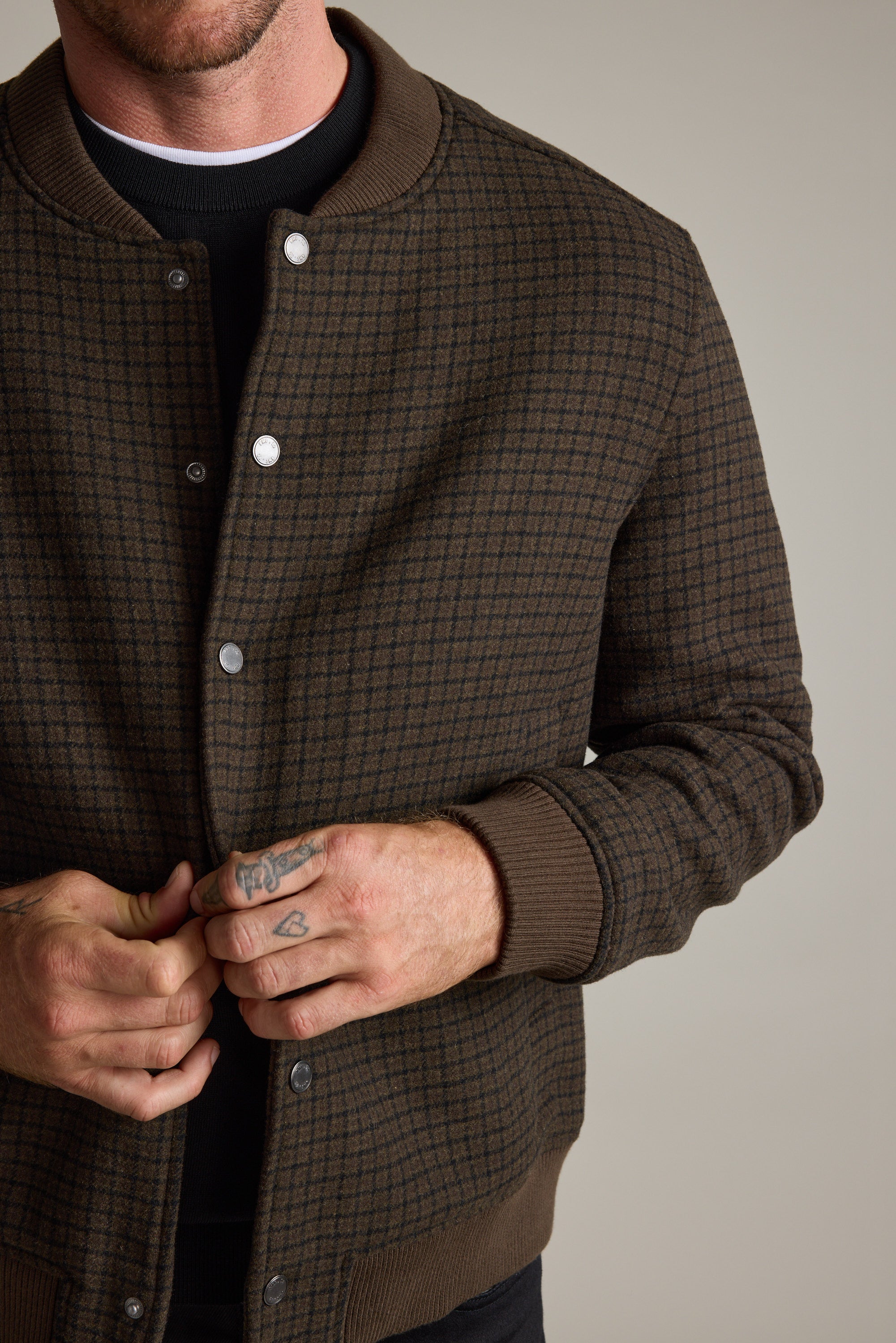 Man buttoning Barkers Leland Wool Bomber Jacket, neutral background.