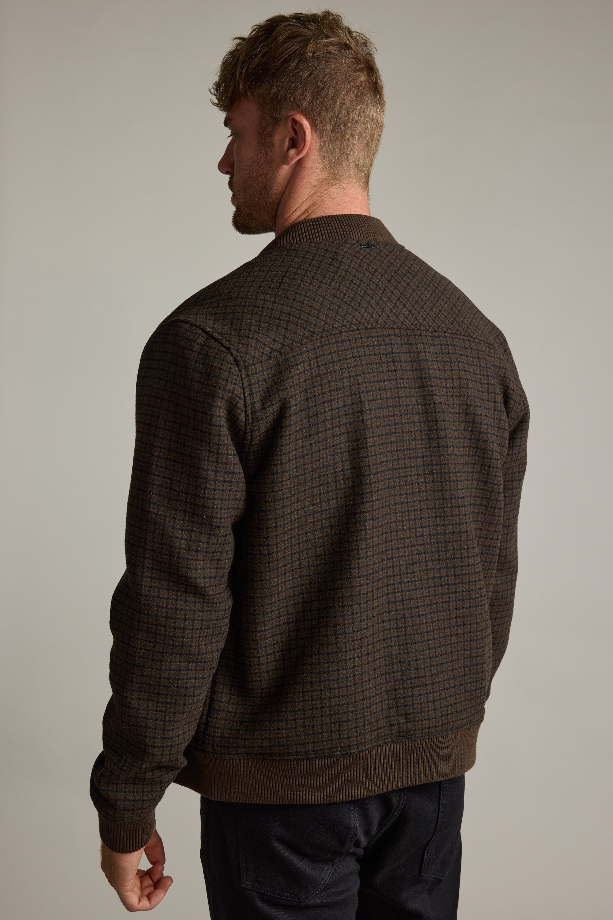 Man facing away in a Barkers Leland Wool Bomber Jacket and dark pants, plain background.
