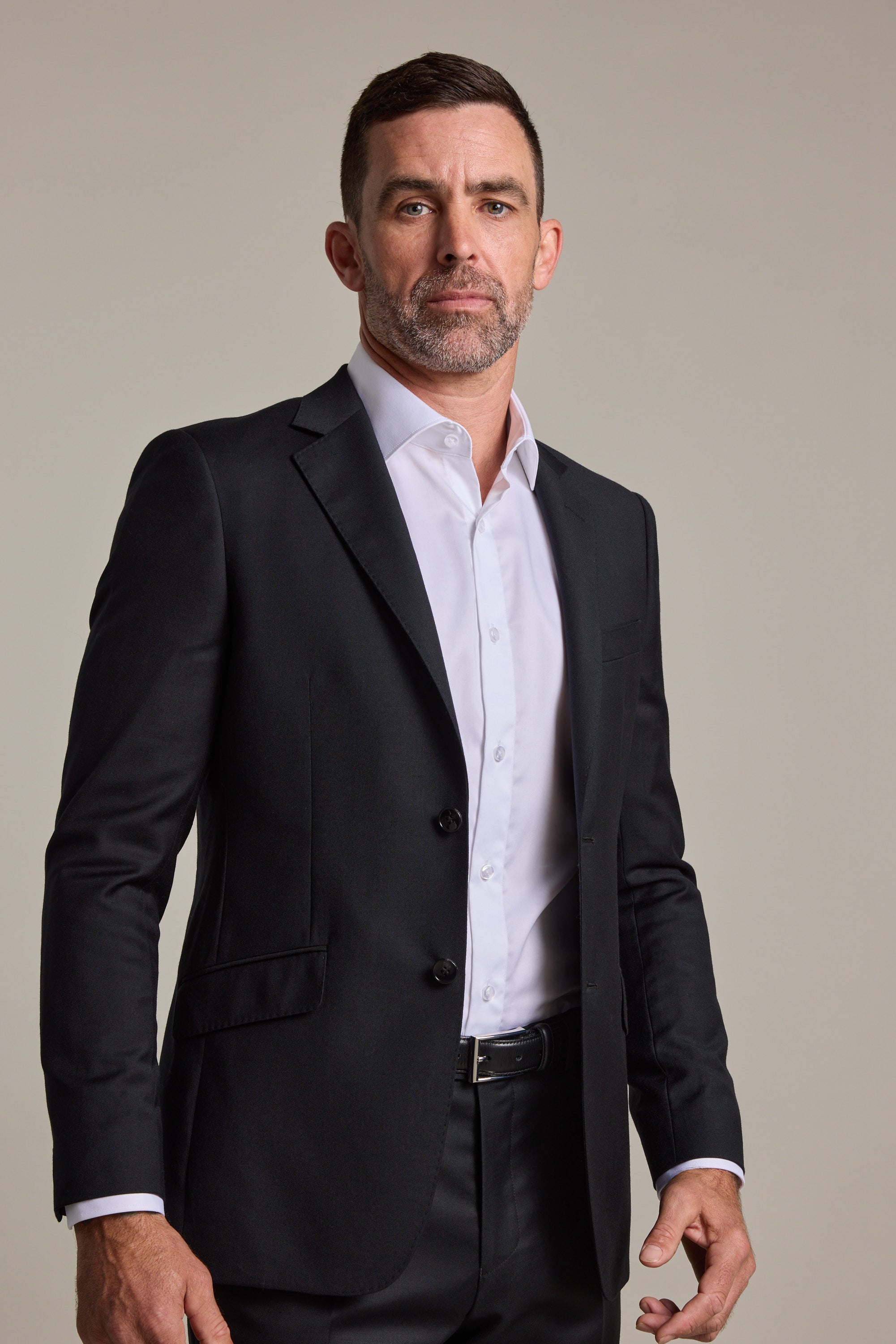 A man with short dark hair and a trimmed beard wears the Barkers Mayfair ZQrx Suit Jacket over a white dress shirt and black pants, standing confidently against a plain light background.