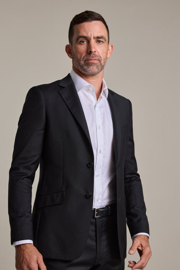 A man with short dark hair and a trimmed beard wears the Barkers Mayfair ZQrx Suit Jacket over a white dress shirt and black pants, standing confidently against a plain light background.