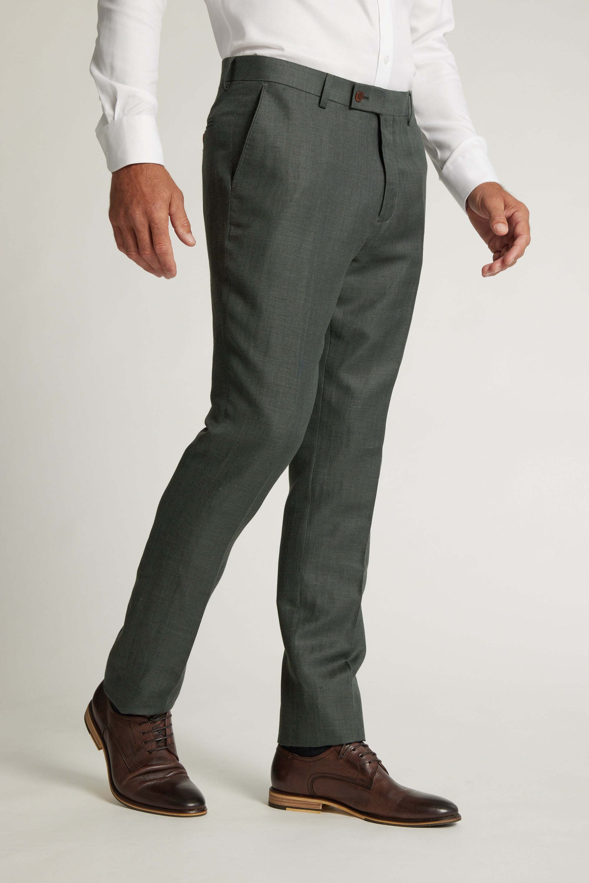 A person wears Barkers Inverness Suit Trouser in dark grey with a white dress shirt and brown leather shoes, standing against a plain light background; the outfit is formal and neatly tailored.