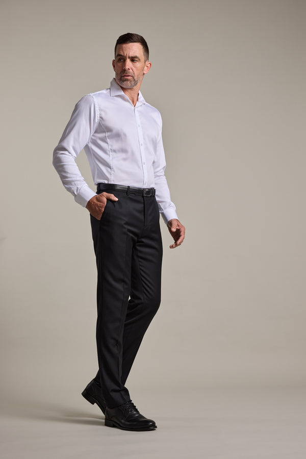 A man wearing a white dress shirt, Barkers Mayfair ZQrx Suit Trouser, and black shoes stands with one hand in his pocket, looking slightly to the side against a plain light background.